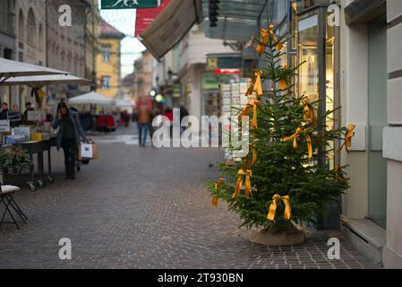 Immergiti nel fascino delle vacanze di una pittoresca piazza della città, adornata da un albero di Natale decorato con vivaci nastri arancione-oro. Il ci festivo Foto Stock