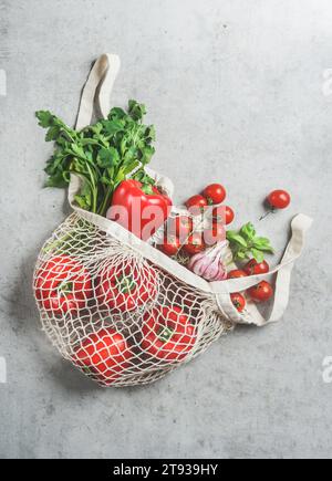 Vista dall'alto di varie verdure ed erbe nella sacca riutilizzabile in plastica gratuita presso il tavolo da cucina grigio in cemento Foto Stock