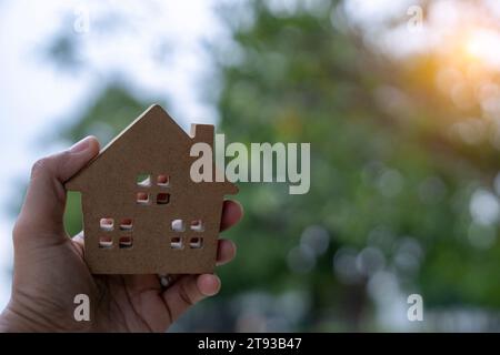 Casa modello in miniatura in mano con sfondo luminoso bokeh Foto Stock