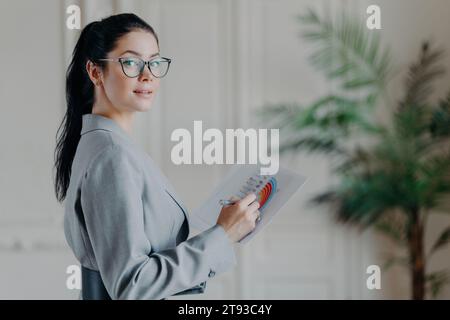 Donna d'affari sicura di sé che analizza un grafico, vestita con un elegante abito grigio, in un ufficio ben illuminato Foto Stock