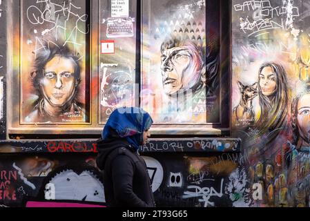 Una donna cammina davanti a un muro coperto di graffiti luminosi e Street art nel quartiere East End di Londra, Regno Unito Foto Stock