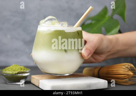 Donna che regge un bicchiere di latte matcha ghiacciato al tavolo di legno grigio, primo piano Foto Stock