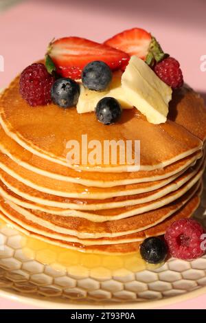 Deliziosi pancake con frutti di bosco freschi, burro e miele su sfondo rosa, primo piano Foto Stock