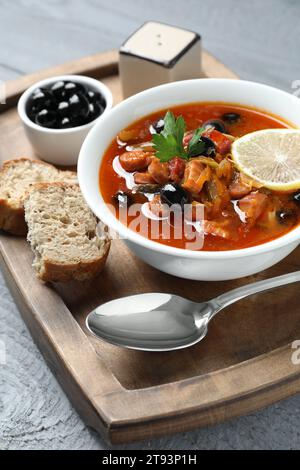 Zuppa di solyanka di carne con salsicce, olive e verdure in ciotola servita su un tavolo di legno grigio, primo piano Foto Stock
