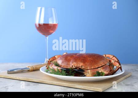 Delizioso granchio bollito servito con verdure e vino al tavolo su sfondo azzurro Foto Stock