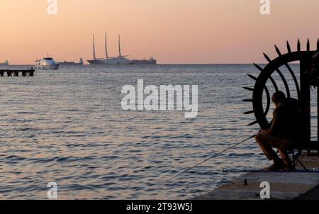 Trieste, Italia – 2023, 19 novembre: Sconosciuto pescatore sul molo di Trieste, sullo sfondo lo yacht A vela A del miliardario Andrey Melnichenko Foto Stock