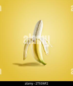 Banana parzialmente sbucciata alla luce del sole su sfondo giallo. Deliziosa frutta tropicale. Vista frontale. Foto Stock