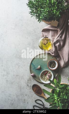 Fondo cucina con vari ingredienti di sapore e condimento su tavola di cemento grigio cucina: Erbe fresche, olio, aglio, salvia, utensili da cucina e. Foto Stock