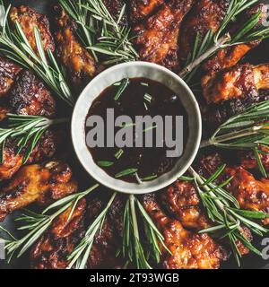 Primo piano delle ali di pollo alla griglia con rosmarino e salsa fatta in casa. Cucina a casa con carne marinata. Deliziosi stuzzichini. Vista dall'alto. Foto Stock