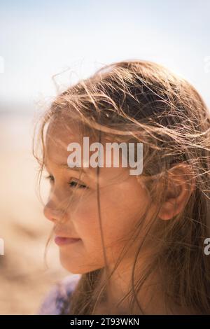 Primo piano di una giovane ragazza con un profilo solare che cattura i fili dei suoi capelli in slitta con un'espressione serena e premurosa Foto Stock