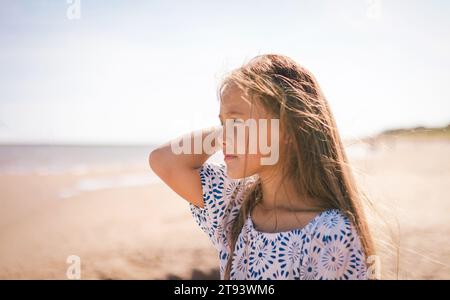 Primo piano di una giovane ragazza con un profilo solare che cattura i fili dei suoi capelli in slitta con un'espressione serena e premurosa Foto Stock