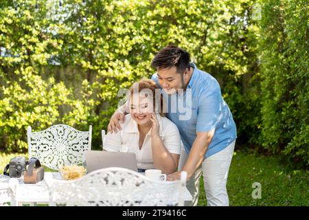 Giovane coppia asiatica chubby utilizzando un computer portatile nel parco verde all'aperto insieme. Felice uomo sorridente e donna che lavorano a distanza e avviare il proprio business insieme Foto Stock