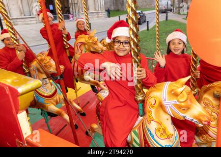 I coristi della Cattedrale di Ely fanno un giro sulla giostra tradizionale al mercatino di Natale della città dopo la pratica del coro mattutino . Foto Stock