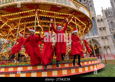 I coristi della Cattedrale di Ely fanno un giro sulla giostra tradizionale al mercatino di Natale della città dopo la pratica del coro mattutino . Foto Stock