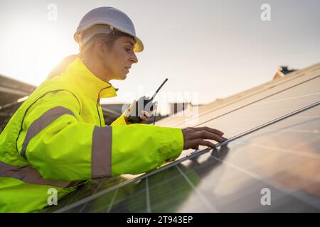 Tecnico solare con walkie-talkie che ispeziona i pannelli solari al crepuscolo. Immagine del concetto ecologico di energia alternativa. Foto Stock