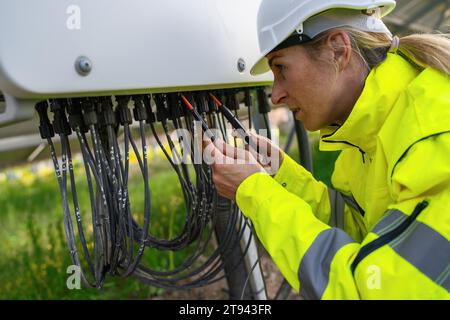 Tecnico che controlla i cavi del pannello solare con un multimetro in un campo di solarpark. Immagine del concetto ecologico di energia alternativa. Foto Stock