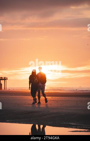 Passeggiata romantica di una giovane coppia sulle spiagge di Ostenda nel Belgio occidentale al tramonto. Amore e devozione. Riflesso in una pozza d'acqua. Foto Stock