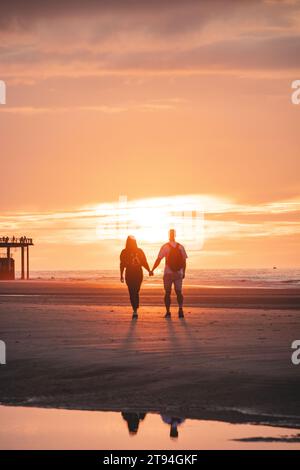 Passeggiata romantica di una giovane coppia sulle spiagge di Ostenda nel Belgio occidentale al tramonto. Amore e devozione. Riflesso in una pozza d'acqua. Foto Stock