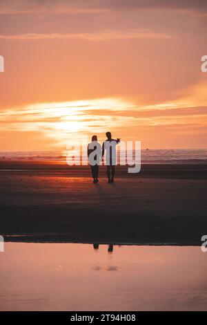 Passeggiata romantica di una giovane coppia sulle spiagge di Ostenda nel Belgio occidentale al tramonto. Amore e devozione. Riflesso in una pozza d'acqua. Foto Stock