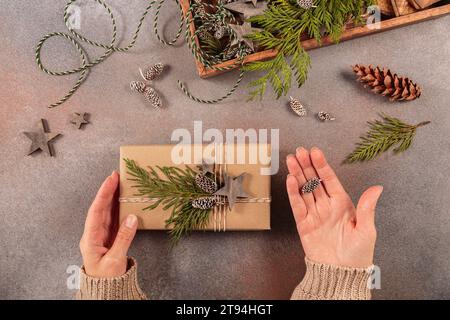 Decorazioni natalizie e mani femminili che decorano la confezione regalo fatta a mano Foto Stock
