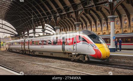 Un moderno treno si trova in una storica piattaforma ferroviaria sotto una tettoia di ferro del XIX secolo. Due membri dell'equipaggio parlano accanto a una colonna. Foto Stock