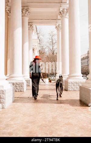 Una foto di una donna e della sua Grande Dane che cammina per una città, ammirando le immagini e i suoni dell'ambiente urbano. Foto Stock