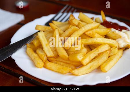 Pommes frites - chiamate anche patatine fritte o patatine fritte - servite con ketchup e condimenti di maionese a lato. Foto Stock