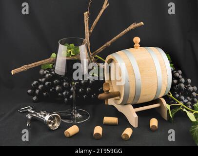 vino rosso di vetro, botte di vino, uva nera, sughero, apribottiglie e edera Foto Stock