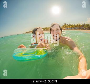 Il padre e il figlio giocosi giocano in mare, creando schizzi giocosi e godendosi le onde Foto Stock