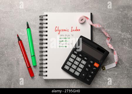 Indice glicemico. Notebook con informazioni, pennarelli, calcolatrice e metro a nastro su tavolo grigio chiaro, posizionamento piatto Foto Stock