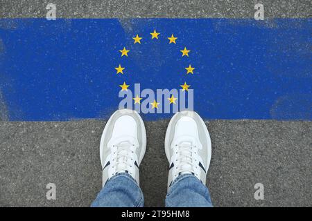 Immigrazione. Uomo in piedi sull'asfalto vicino alla bandiera dell'Unione europea, vista dall'alto Foto Stock