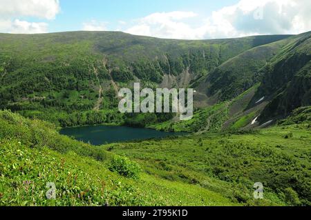 Un bellissimo laghetto in una profonda conca dell'intermountain con neve sulle piste e sponde sotto un soleggiato cielo estivo. Laghi di Ivanovskie, Khakassia, Siberia, Foto Stock