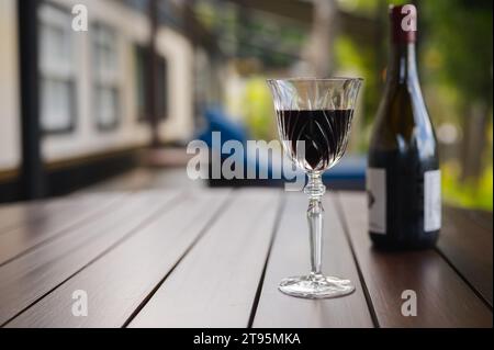 Un bicchiere di vino rosso con una bottiglia sul tavolo di legno sul balcone della casa per godersi un momento di relax. Foto Stock