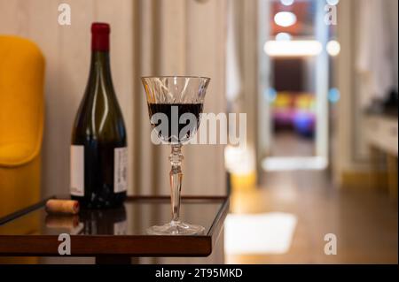 Un bicchiere di vino rosso con una bottiglia sul tavolino della casa per godersi un momento di relax. Foto Stock