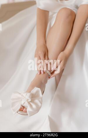 La sposa in abito bianco irriconoscibile le mette una scarpa da sposa sul piede. Bellezza e stile. Verticale. Foto Stock