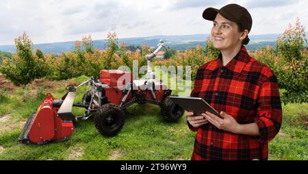 L'agricoltore controlla la trebbiatrice automatica autonoma con il braccio robotico che raccoglie le mele in un'azienda agricola intelligente. Concetto. Foto Stock