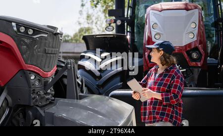 Agricoltore donna con un tablet digitale accanto al trattore agricolo. Foto Stock