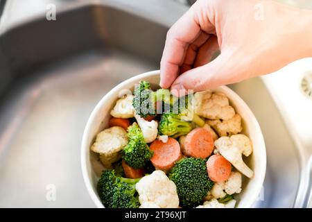 Vista dall'alto di prendere a mano verdure tritate da un recipiente pieno di broccoli, cavolfiori e carote. Foto Stock