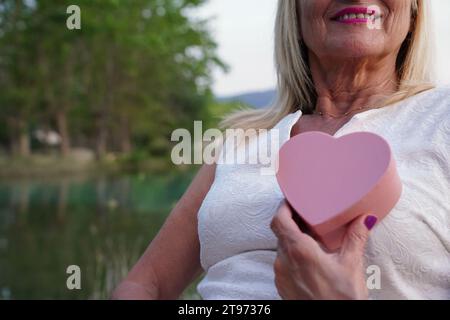 Ritratto ravvicinato di una donna anziana vitale irriconoscibile che tiene una forma di cuore presente durante San Valentino Foto Stock