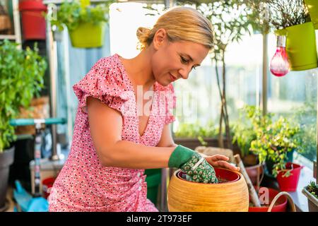 La donna felice ama fare giardinaggio sul balcone di casa sua. Sta mettendo la terra nel vaso dei fiori. Foto Stock