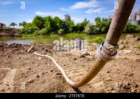 Tubo flessibile antincendio lungo con raccordo metallico posizionato sulla costa del fiume nel cantiere per l'approvvigionamento idrico, la costruzione di ponti è in corso. Foto Stock