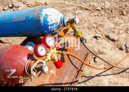 Apparecchiature di saldatura rosse e blu, serbatoi di ossigeno e azoto con valvole e manometri, bombole di gas acetilene posizionate su pali metallici all'interno della struttura Foto Stock