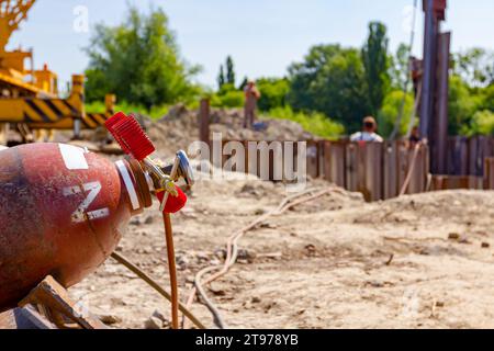 Apparecchiature di saldatura rosse e blu, serbatoi di ossigeno e azoto con valvole e manometri, bombole di gas acetilene posizionate su pali metallici all'interno della struttura Foto Stock