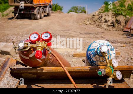 Apparecchiature di saldatura rosse e blu, serbatoi di ossigeno e azoto con valvole e manometri, bombole di gas acetilene posizionate su pali metallici all'interno della struttura Foto Stock