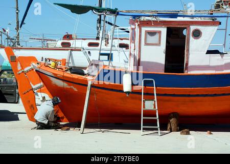 Un pescatore greco di Ikaria dipinge la sua barca nel villaggio di pescatori e nel porto di Gialiskari, sulla costa settentrionale dell'isola di Ikaria, una "zona blu" in Grecia. Foto Stock