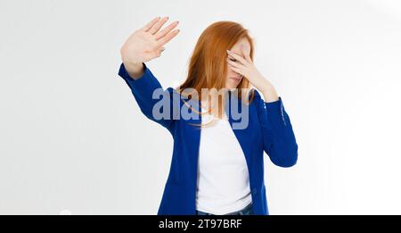 Giovane donna dai capelli rossi che fa una posa di rifiuto e palma del viso su sfondo bianco. Emozione umana negativa espressione del volto sensazione di linguaggio del corpo Foto Stock