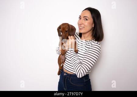 Foto di un simpatico cane da abbraccio millenario che indossa una camicia a righe isolata su sfondo di colore bianco Foto Stock