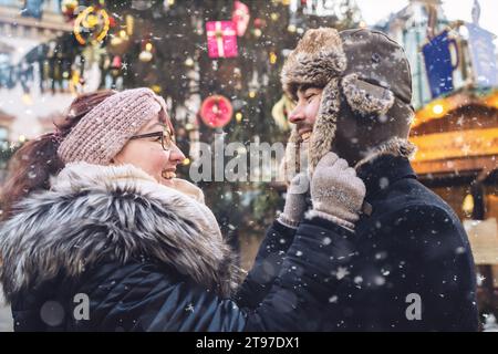 Coppia in abiti invernali che sorridono a vicenda, in una giornata invernale innevata al mercatino di natale Foto Stock