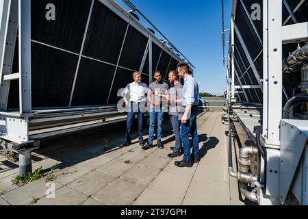 Uomini d'affari e dipendenti che tengono una riunione sul tetto accanto all'impianto di refrigerazione Foto Stock