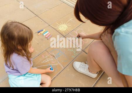 Madre e figlia che disegnano su un pavimento piastrellato al parco Foto Stock